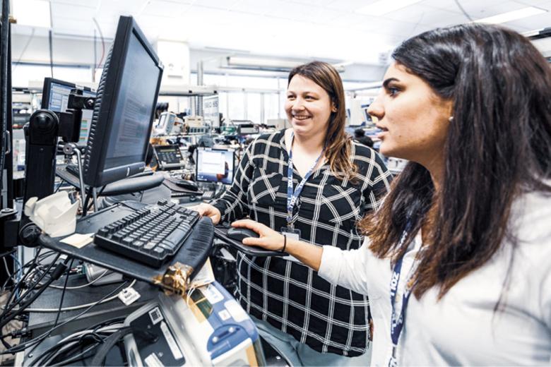 2 Women at a standing desk look at a computer
