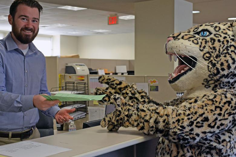 Leopard mascot accepting paper from man behind a counter.