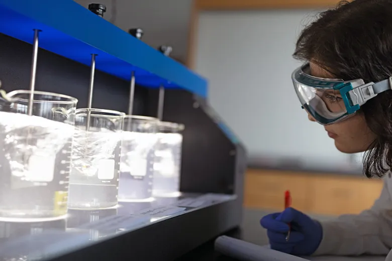 Woman conducting tests in lab, recording results in notebook.