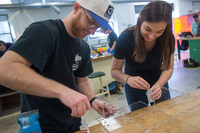 Two students working on engineering project with plexiglass