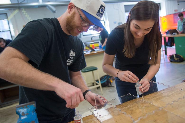 Two students working on engineering project with plexiglass