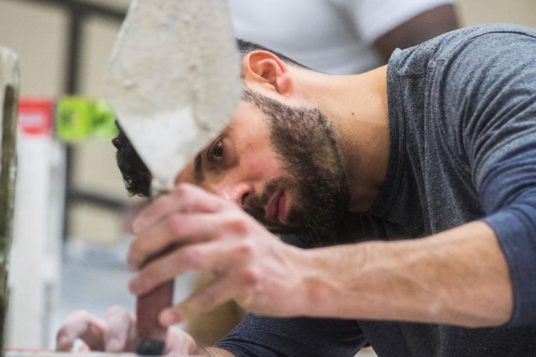 A bearded man uses a trowel to complete a construction project.