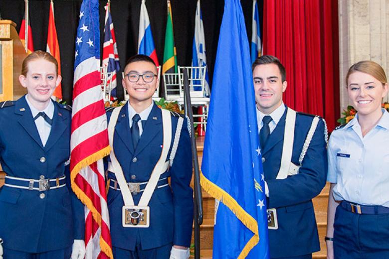 Four students, 2 male and 2 female, in military regalia pose for a photo. 