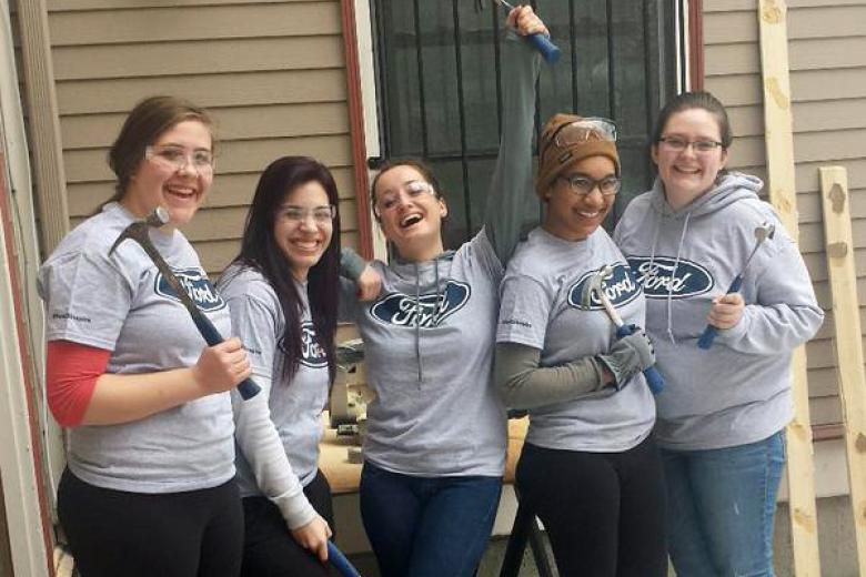 A group of female students holding hammers at building site.