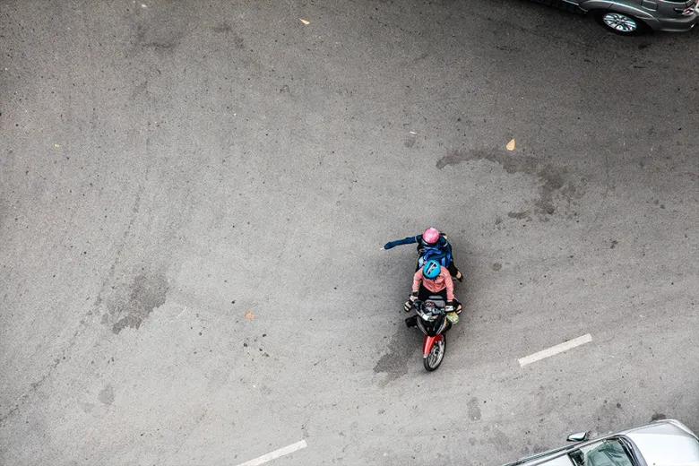 An overhead view of two people on a scooter in the road. 
