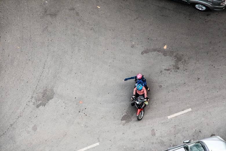 An overhead view of two people on a scooter in the road. 