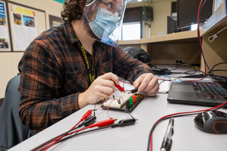 A student connects wires in front of a computer