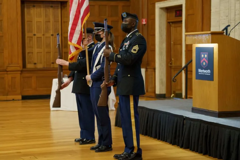 Three uniformed color guard present the American flag. 