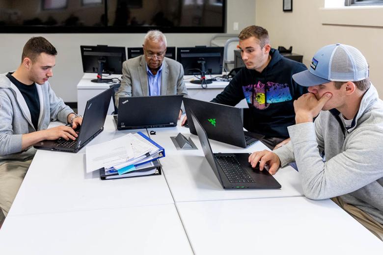 Students and professor around table at laptops