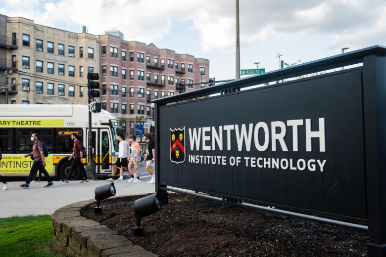 A sign for the Wentworth Institute of Technology is in the foreground and a city bus letting off students is in the background