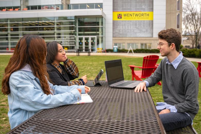 Transfer Students sit at a picnic table on the quad talking - in the background is Beatty Hall