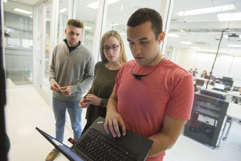 three students looking at laptop while standing
