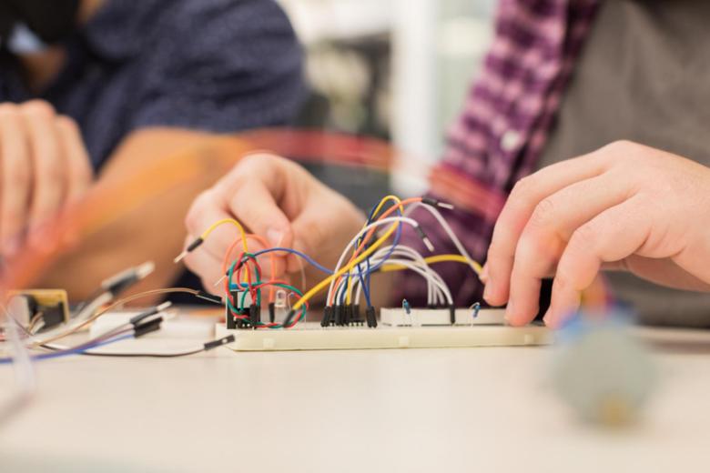 Two students work on a breadboard with wires and electrical components