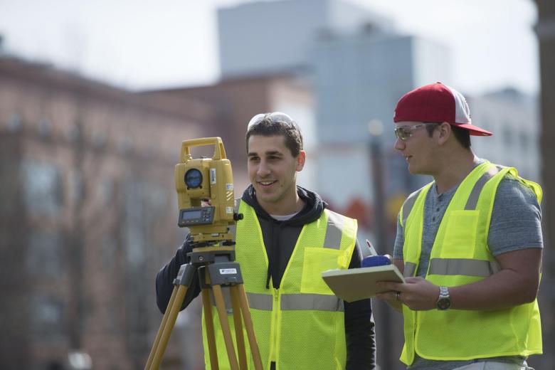 Two students wearing bright vests practice surveying in Boston
