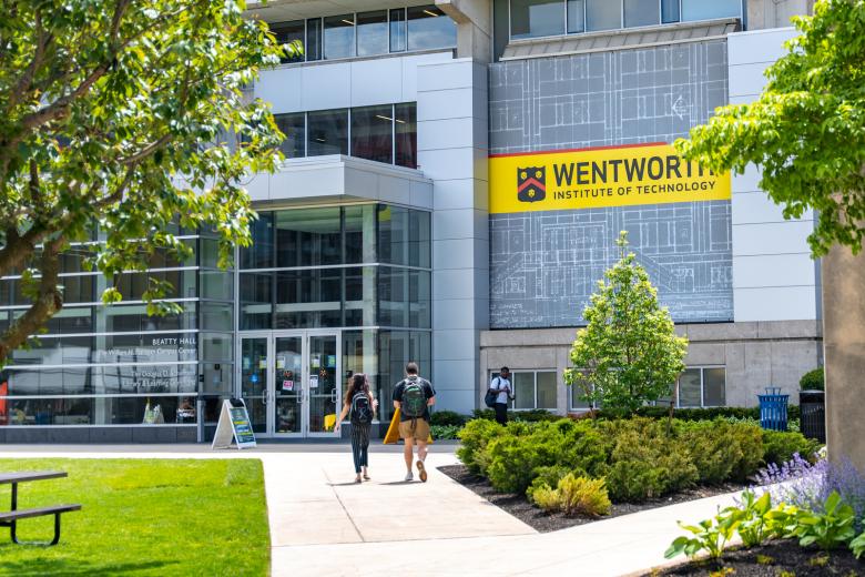 Two students walk towards Beatty Hall in the background with campus greenery in the foreground