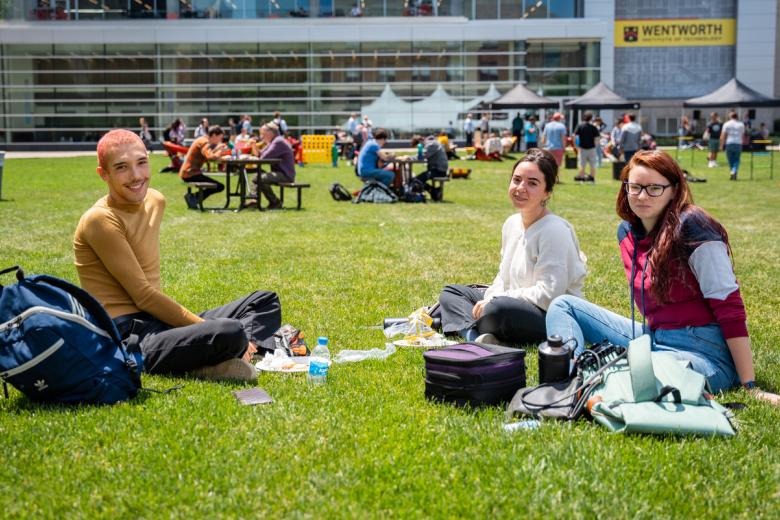 Three students sit on the quad and enjoy at barbecue on a sunny day