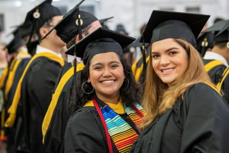 Photo of 2 women smiling and wearing caps and gowns at commencement