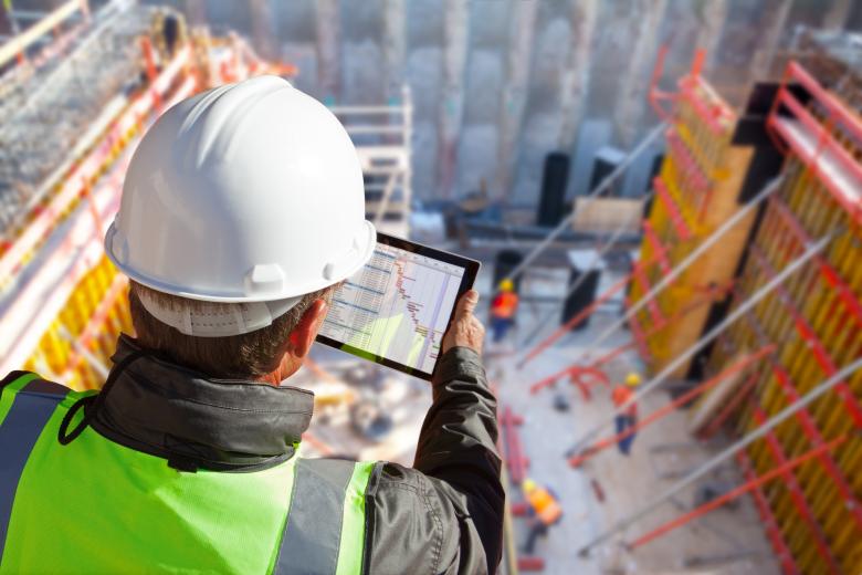 construction worker looking at a gant chart an iPad overseeing a commercial building construction zone