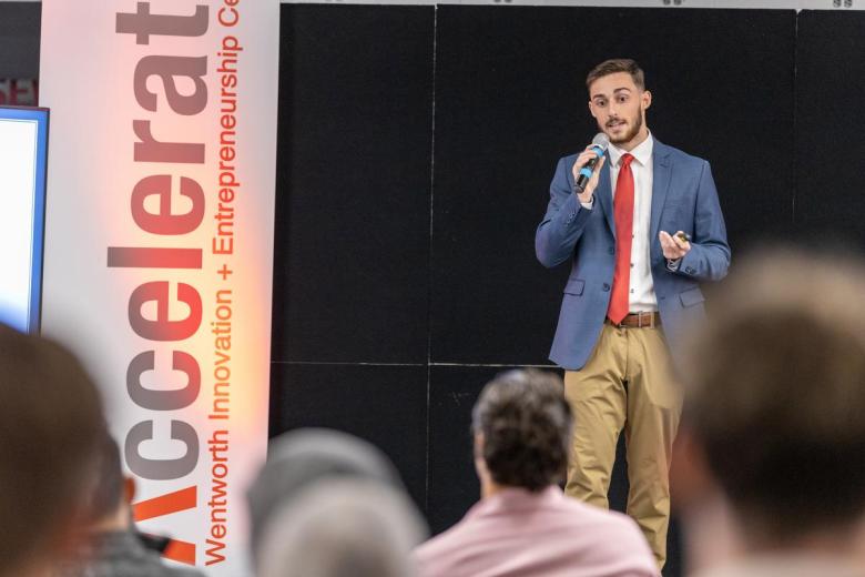 Student speaking into a microphone during a crowded Accelerate Pitch Event