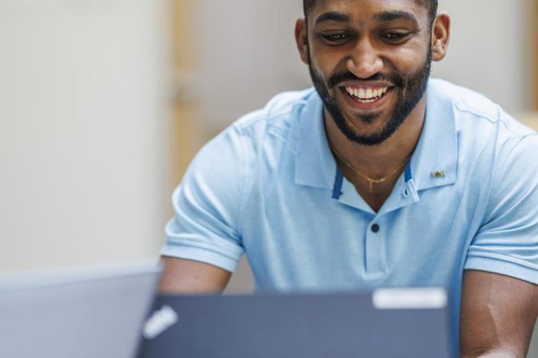 A Wentworth student of color smiles while looking at his laptop.