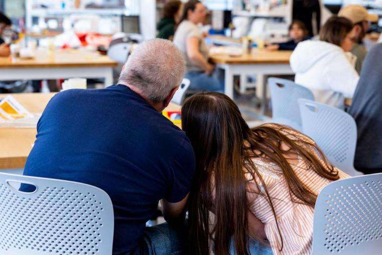 A father and daughter lean their heads together as they work on a project at the Open House