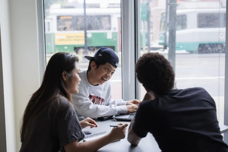 Three students discuss topics while sitting around their laptops