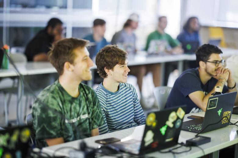 Three students sit in front of their laptops in a classroom