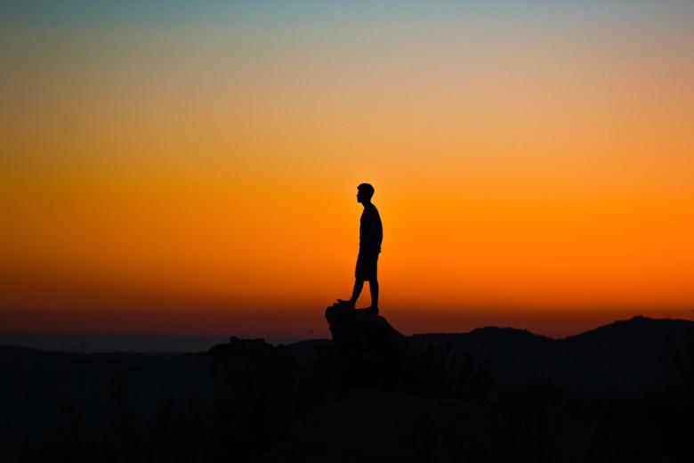 Solitary person on top of hill with sunset