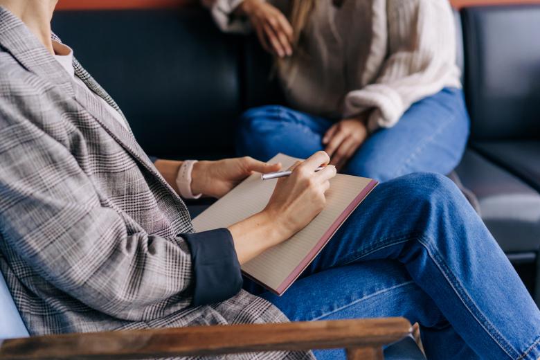two people having a conversation on a couch, one has a notepad, you can't see either of their heads