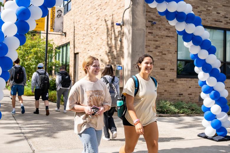 Two students walk underneath a balloon arch heading away from the Wentworth quad.