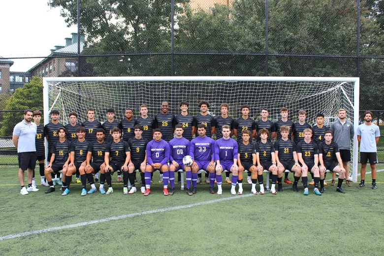 The men's soccer team poses in front of a goal on the soccer field