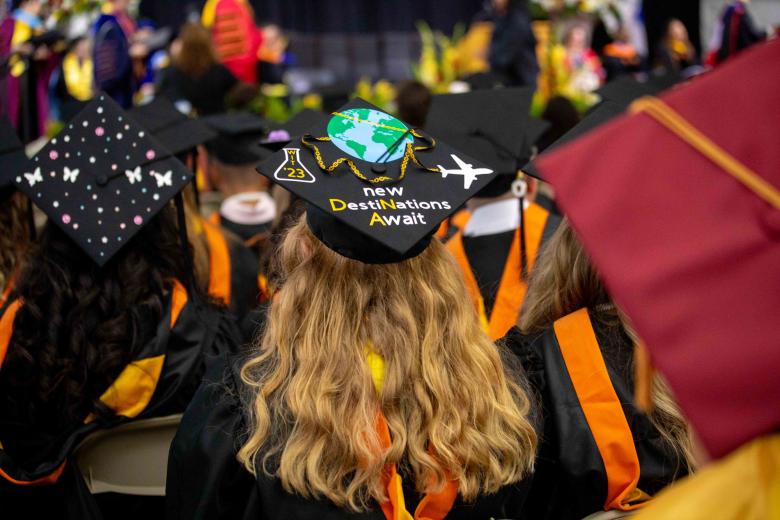 A student wears a cap and gown at graduation that says "new destinations await"
