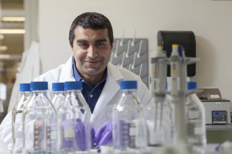 Salil Desai smiles behind a row of beakers