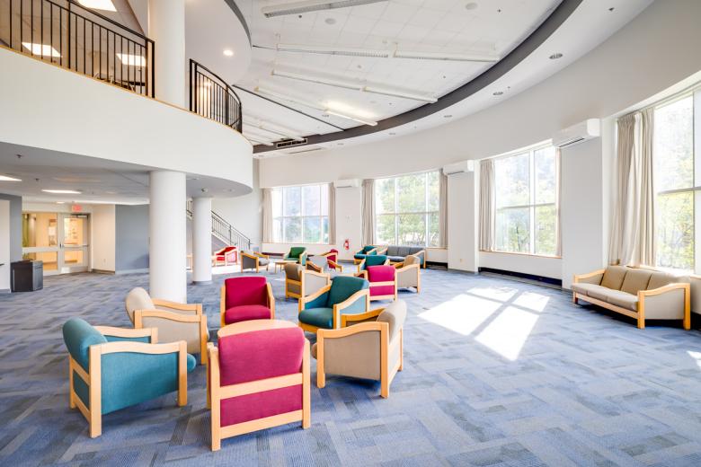 The lobby of the 610 residence hall with chairs, and tall rows of windows facing the outside