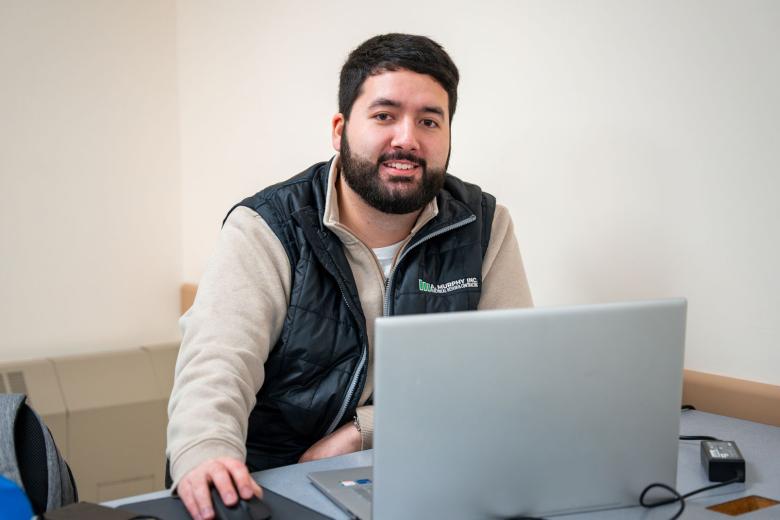 A male adult learner sits at a laptop and smiles
