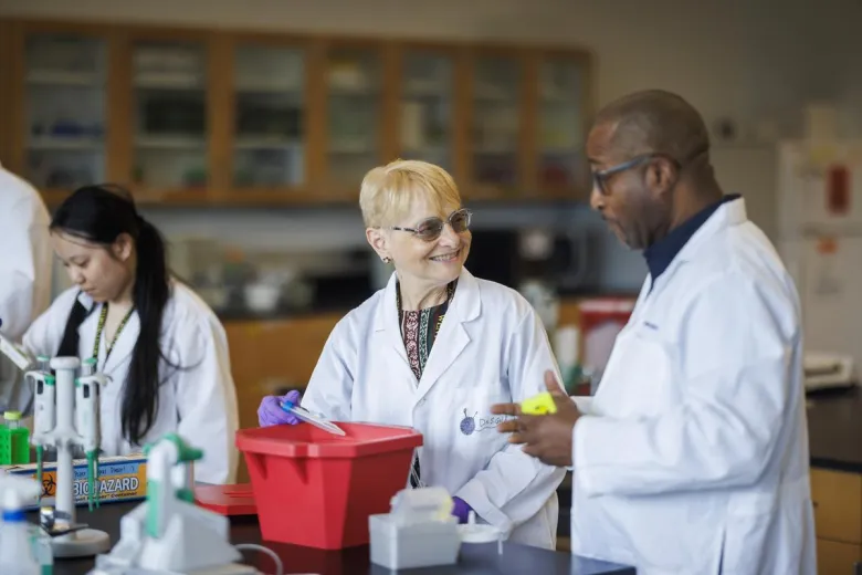 Two faculty members in white coats in the science lab performing an experiment for their students