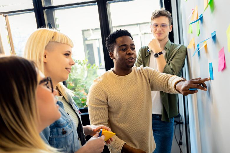 Diverse group of young business people working in office using colorful sticky notes on wall to organize their ideas.