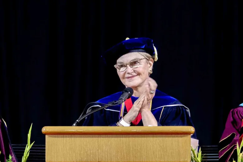 woman in graduation robe speaking at podium