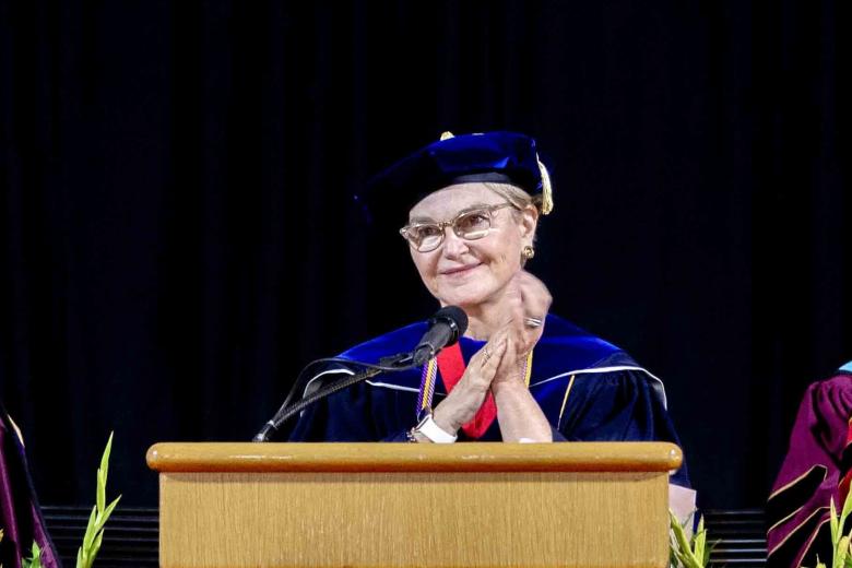 woman in graduation robe speaking at podium
