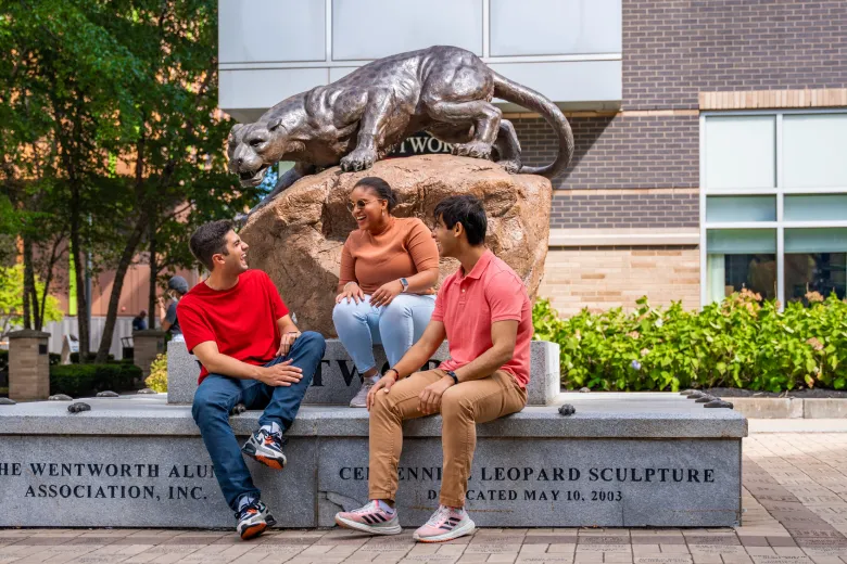 Three students laugh while sitting on the base of the Wentworth Leopard Statue