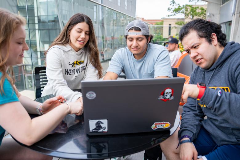 Four students having a conversation with a laptop open