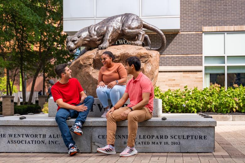 Three students talking enthusiastically in front of Leopard statue.