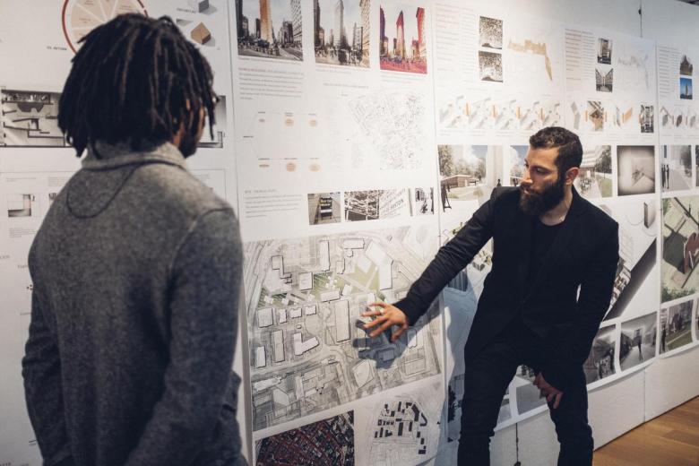 Two architecture students discuss a design pinned to the wall