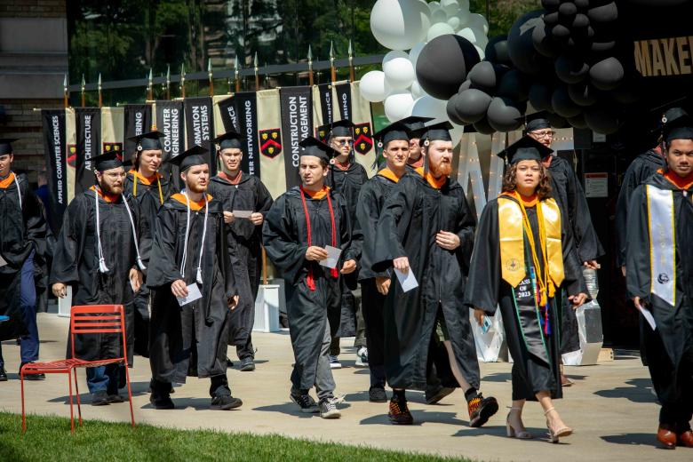 Group of men and women wearing black graduation caps and gowns walking towards their graduation ceremony. 