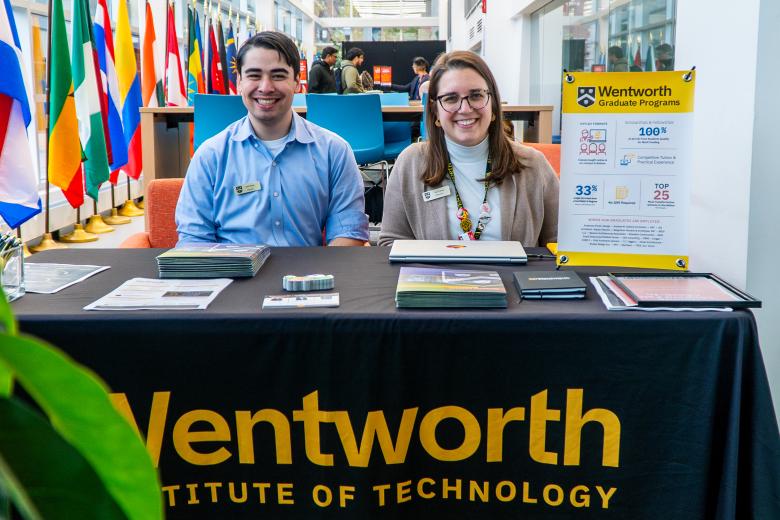 Two Graduate Admissions Counselors sit at a table at the entrance to the admissions event.