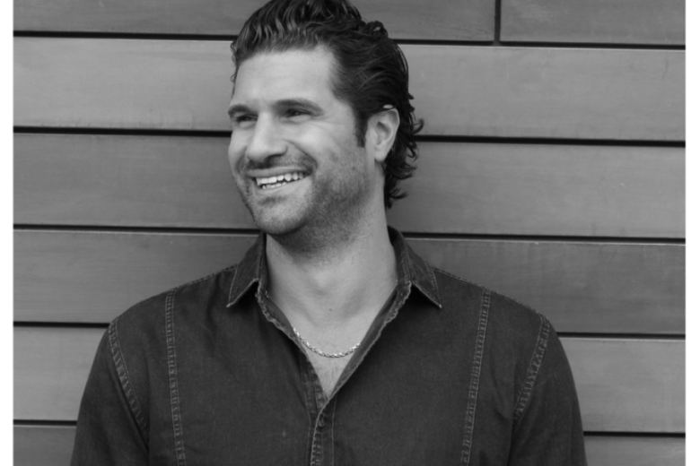 Man smiling looking to the left wearing a dark shirt.