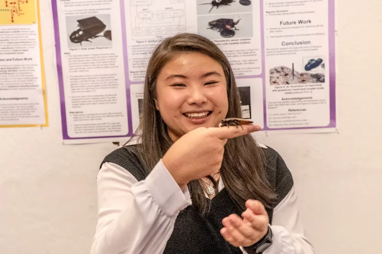 a woman holds up a cockroach fitted with a sensor