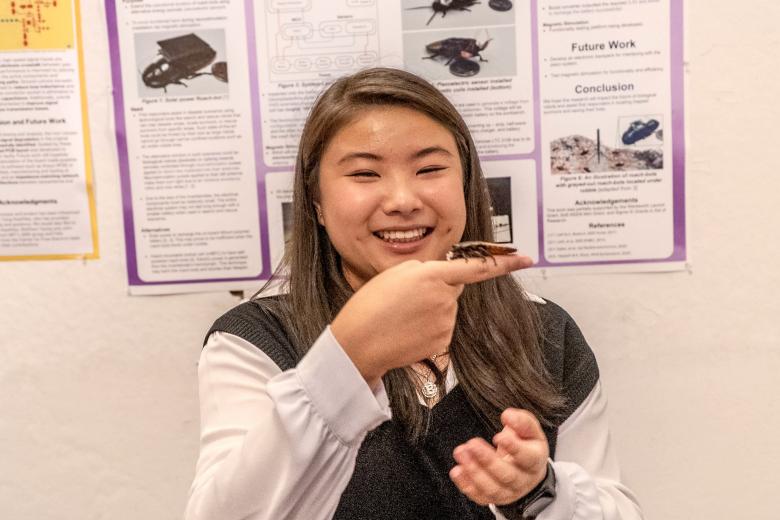 a woman holds up a cockroach fitted with a sensor