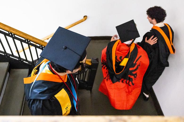 students walking on a staircase with graduate regalia