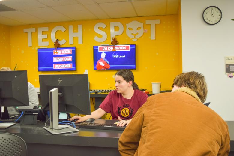 A staff member at a help desk assisting someone on the other side of a computer